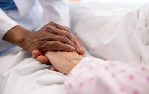 Close-up on a doctor holding the hand of a sick woman in bed at the hospital